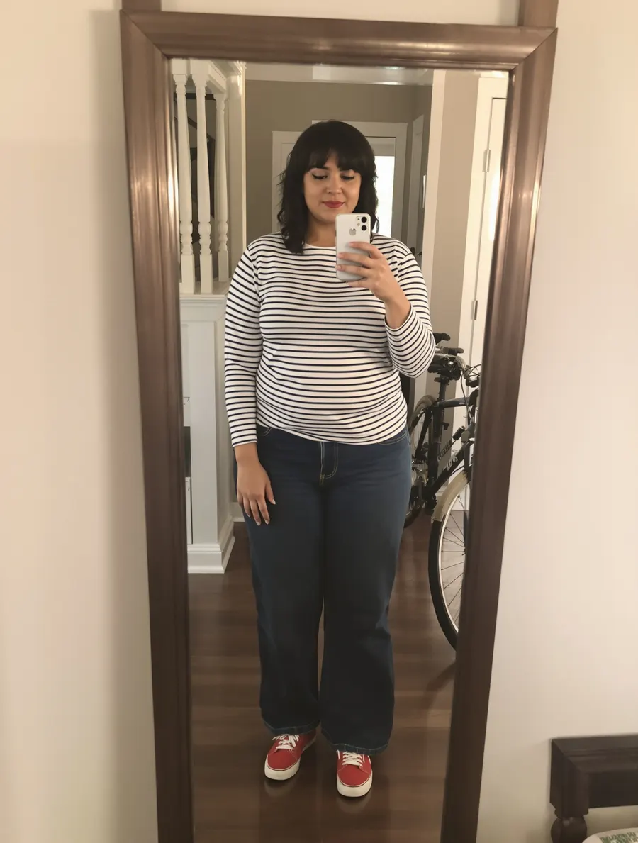 Woman in a striped tee, wide-leg jeans and red sneakers in an entryway mirror